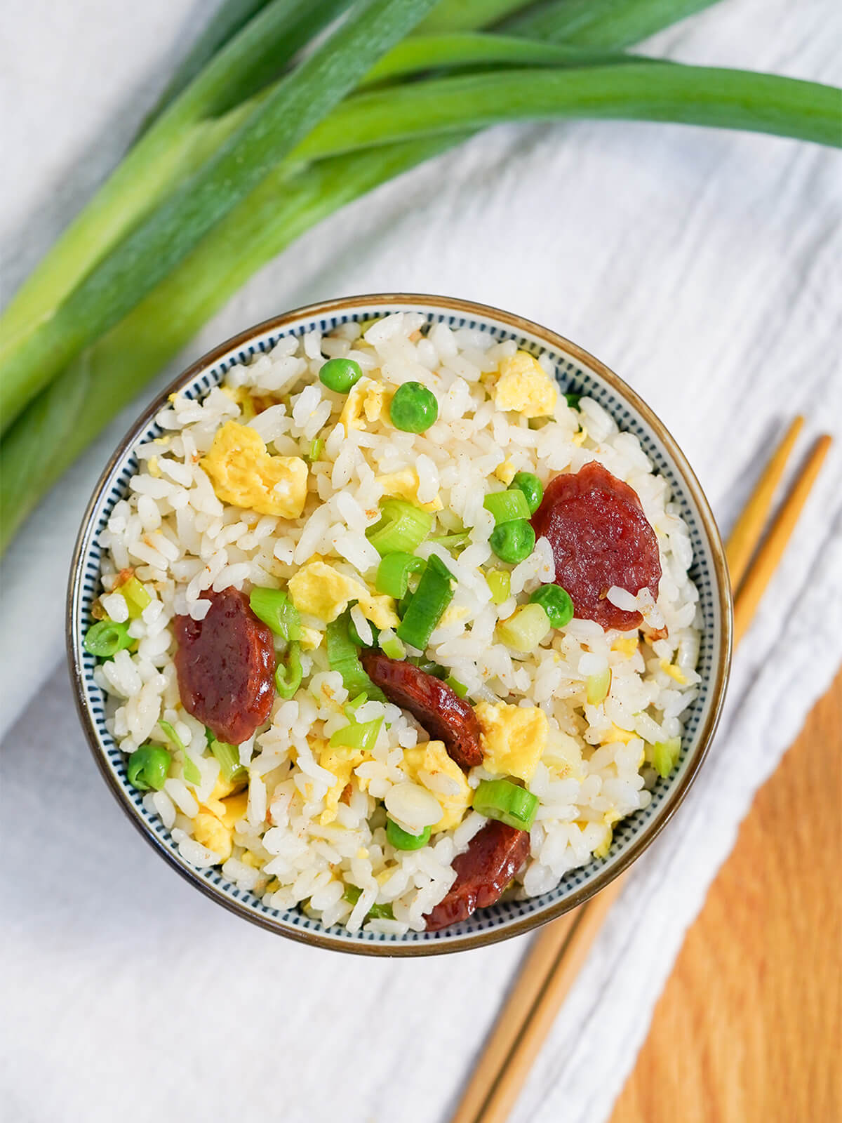 overhead view of bowl of Taiwanese fried rice with chopsticks below bowl and scallion stems to side.