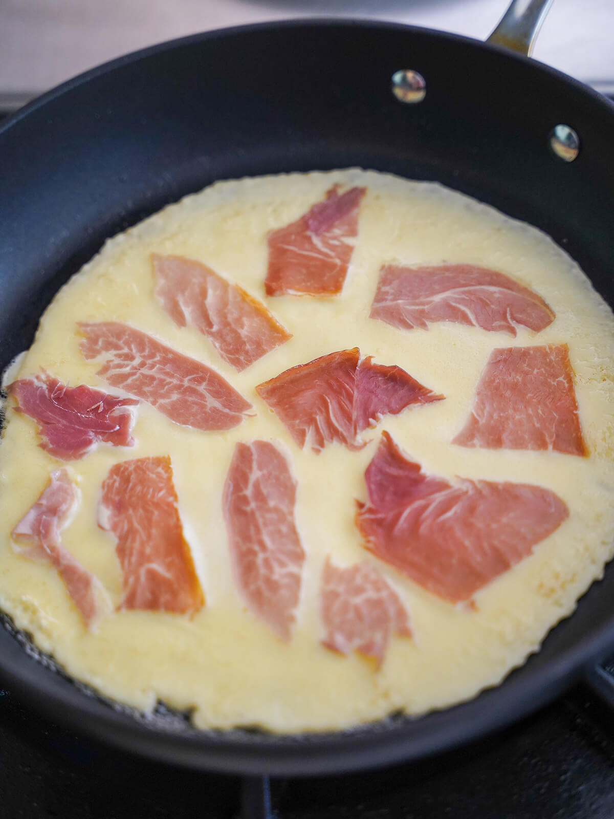 adding speck into Pannekoek, Dutch pancake, as it cooks pieces of speck on top of part cooked pancake.