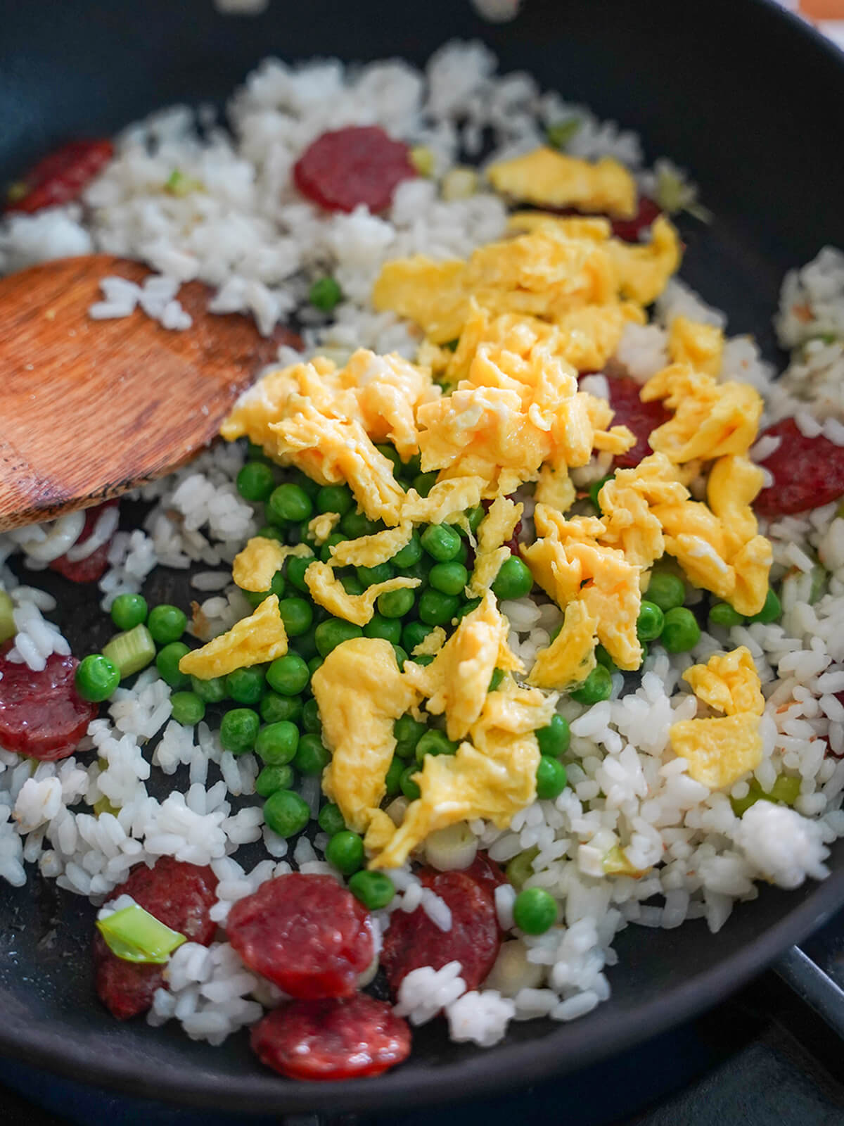 rice, slices of sausage in pan with peas and egg pieces on top and spatula to side.