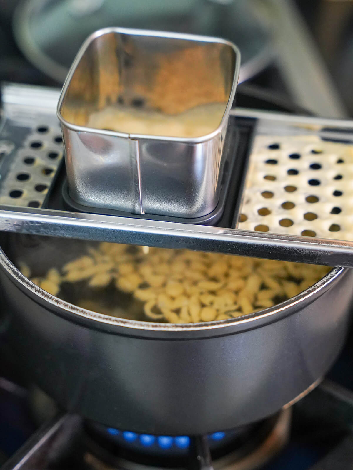 making herb spaetzle speatzle maker over pot of water with some spaetzle floating in water in pot.