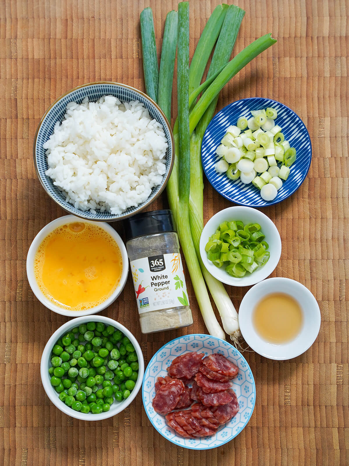 bowls of rice, egg, peas, sliced sausage, scallions with jar white pepper in middle.