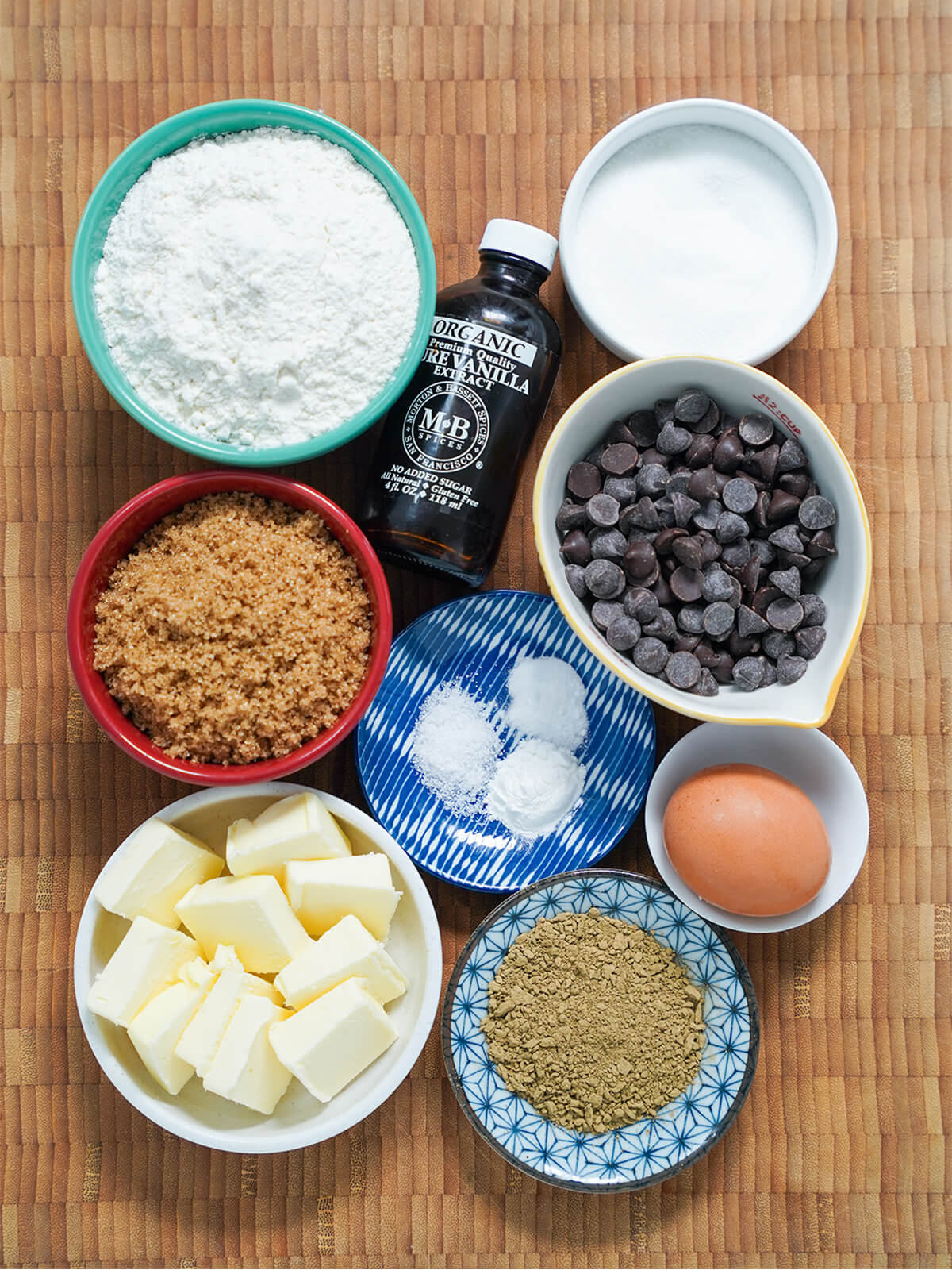 bowls of sugars, flour, chocolate chips, butter, hojicha powder, egg and bottle of vanilla.