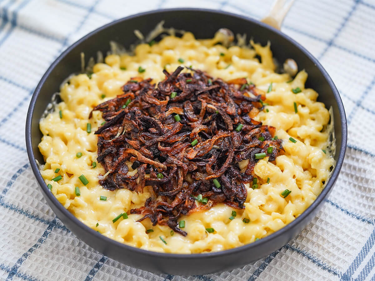 skillet of kaesespaetzle cheese spaetzle topped with caramelized onions.