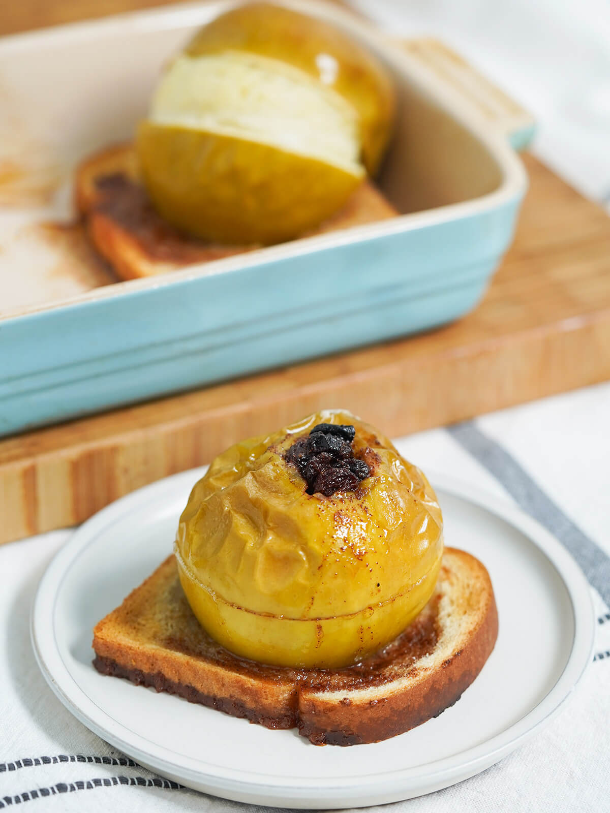 raisin stuffed baked apples - one on plate with other in baking dish behind.